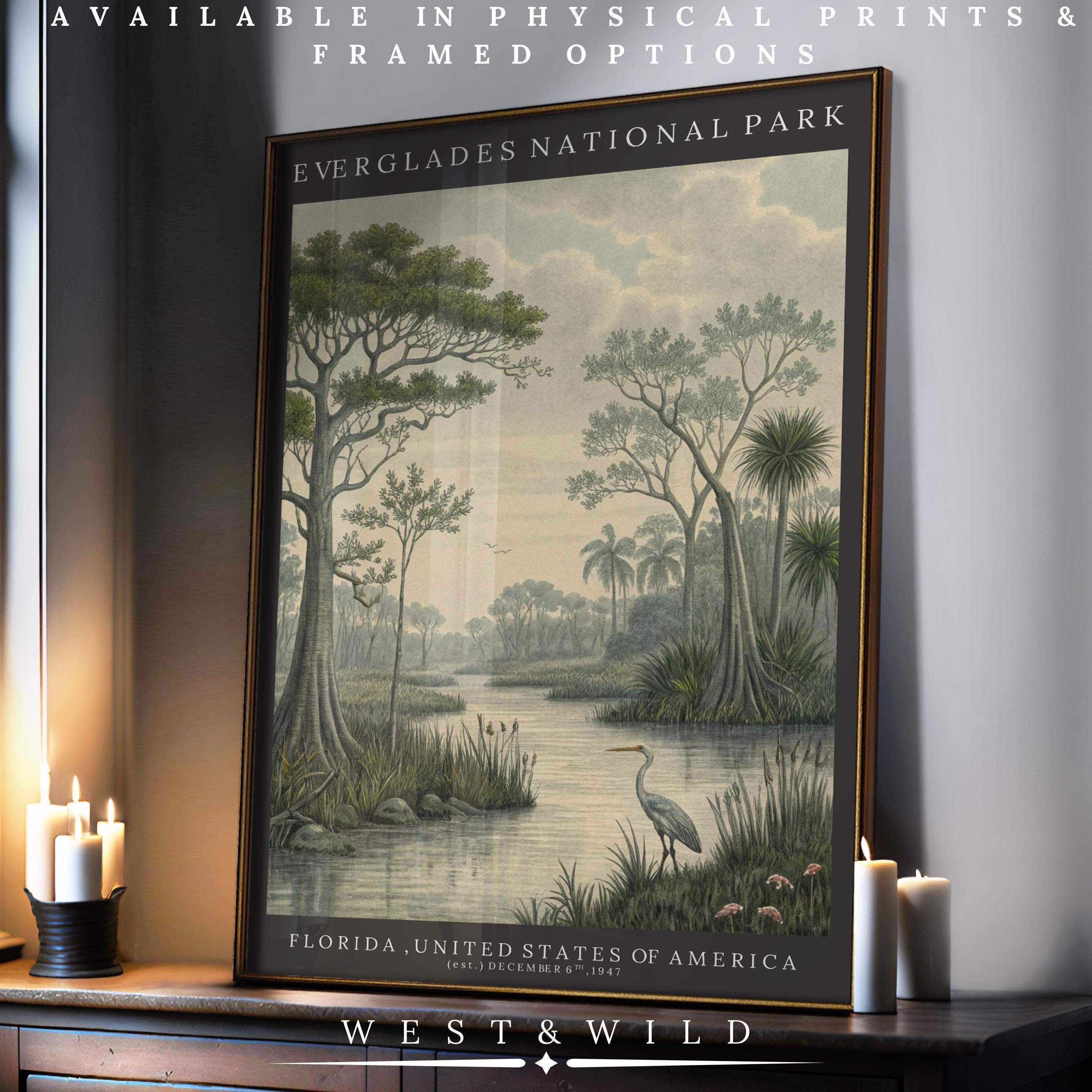 A framed Everglades National Park print rests on a table by lit candles, showing a scenic river, trees, and a heron. Text above and below mentions physical prints and framing options.