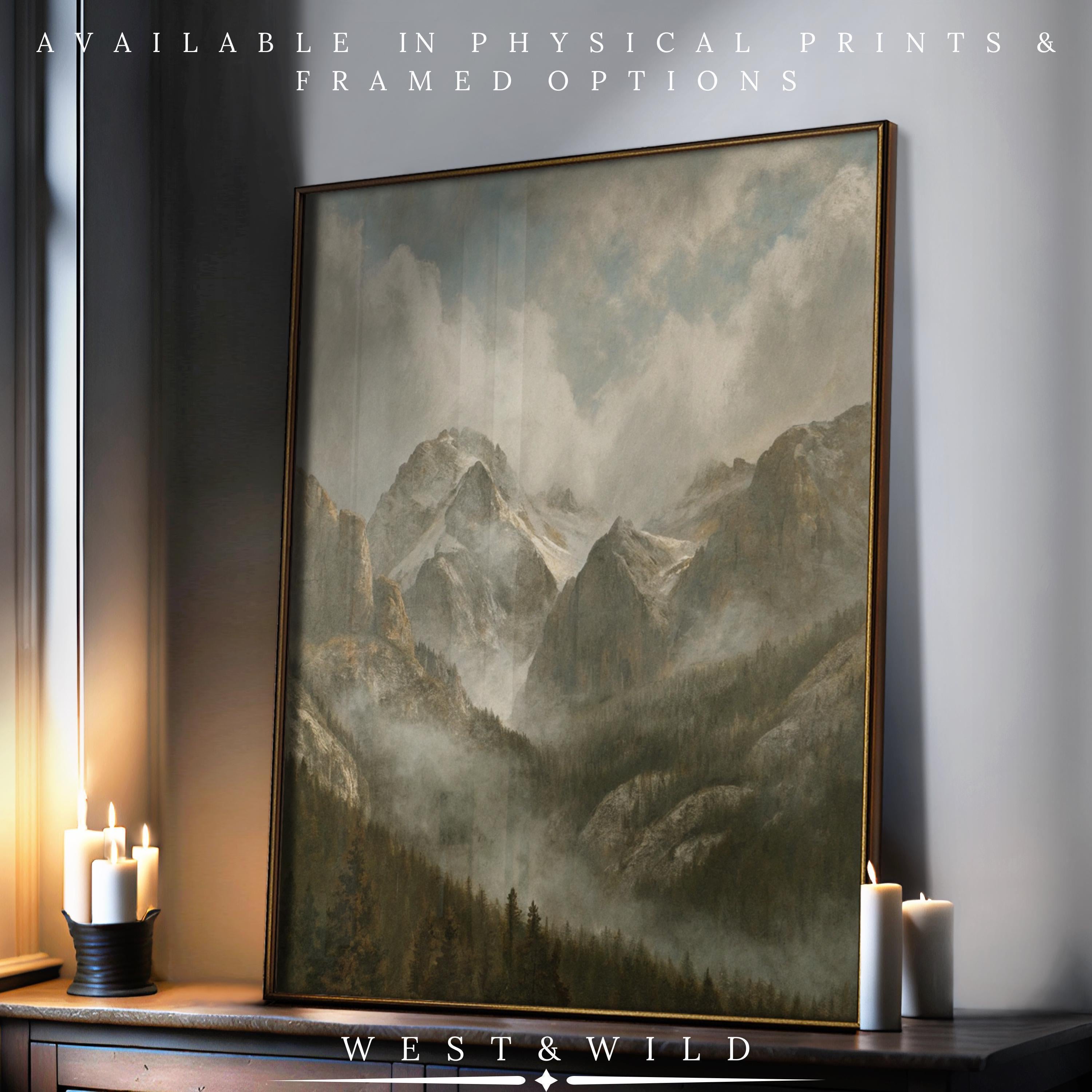 A framed "Rocky Mountain Wall Art - Misty Alpine Print" with pine trees sits on a dark wooden surface near lit white candles in soft light. Available as archival quality prints & framed art. West & Wild Art Archive. Ideal cabin decor gift.