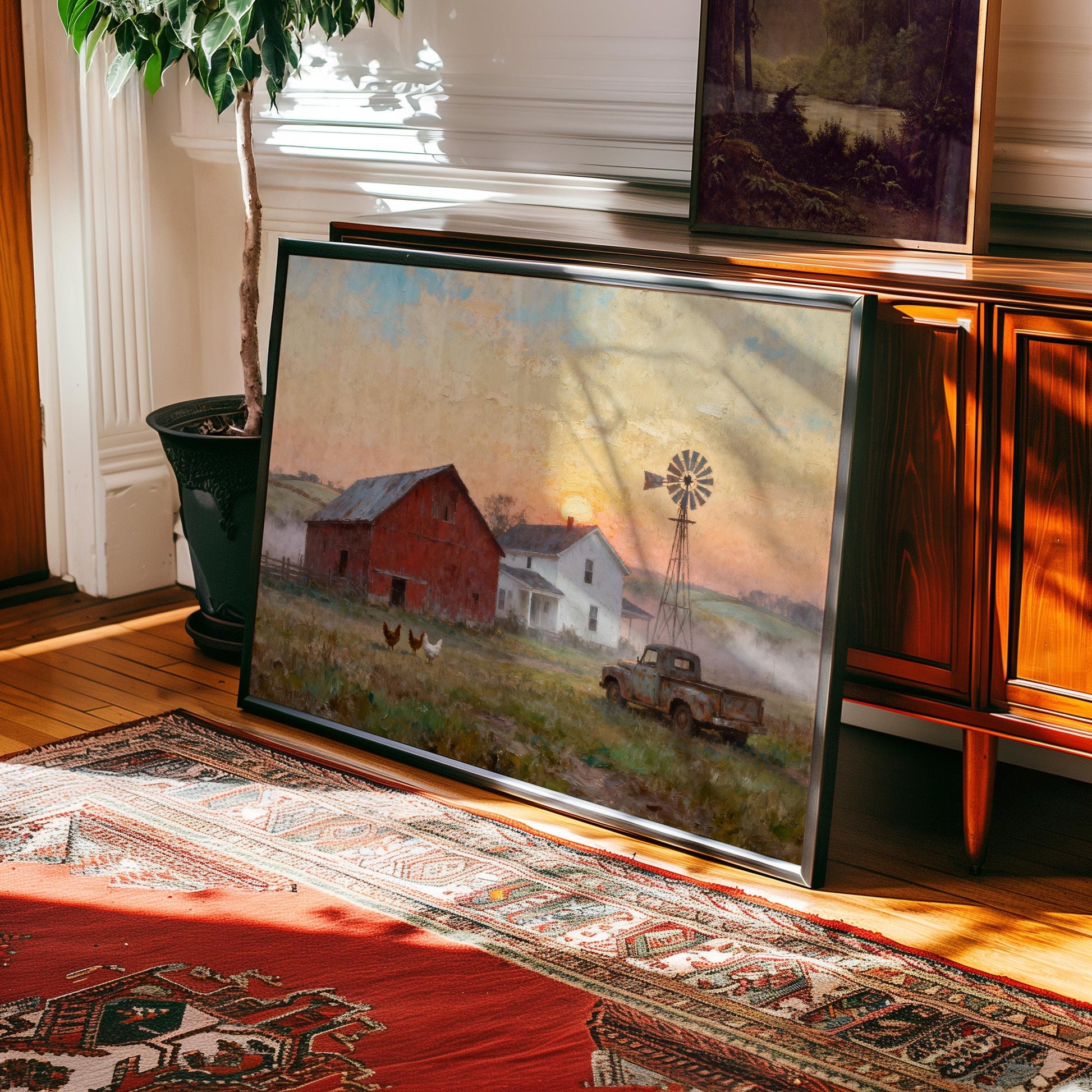 The Rustic Farmhouse Art Print – Red Barn Sunrise Scene with Chickens rests framed against a wooden cabinet on a patterned rug, sunlight streaming in, creating a cozy vintage decor accent. Available framed or unframed.