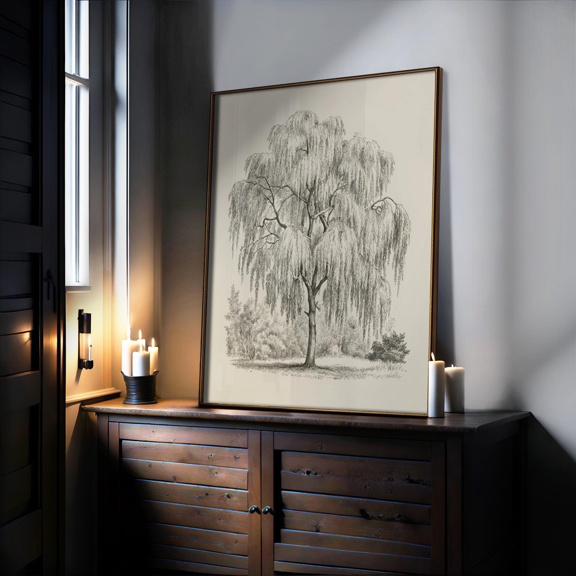 a large framed drawing of a willow tree with long, drooping branches, placed on a wooden cabinet or dresser. The cabinet has a light source on it, creating a warm and cozy atmosphere.