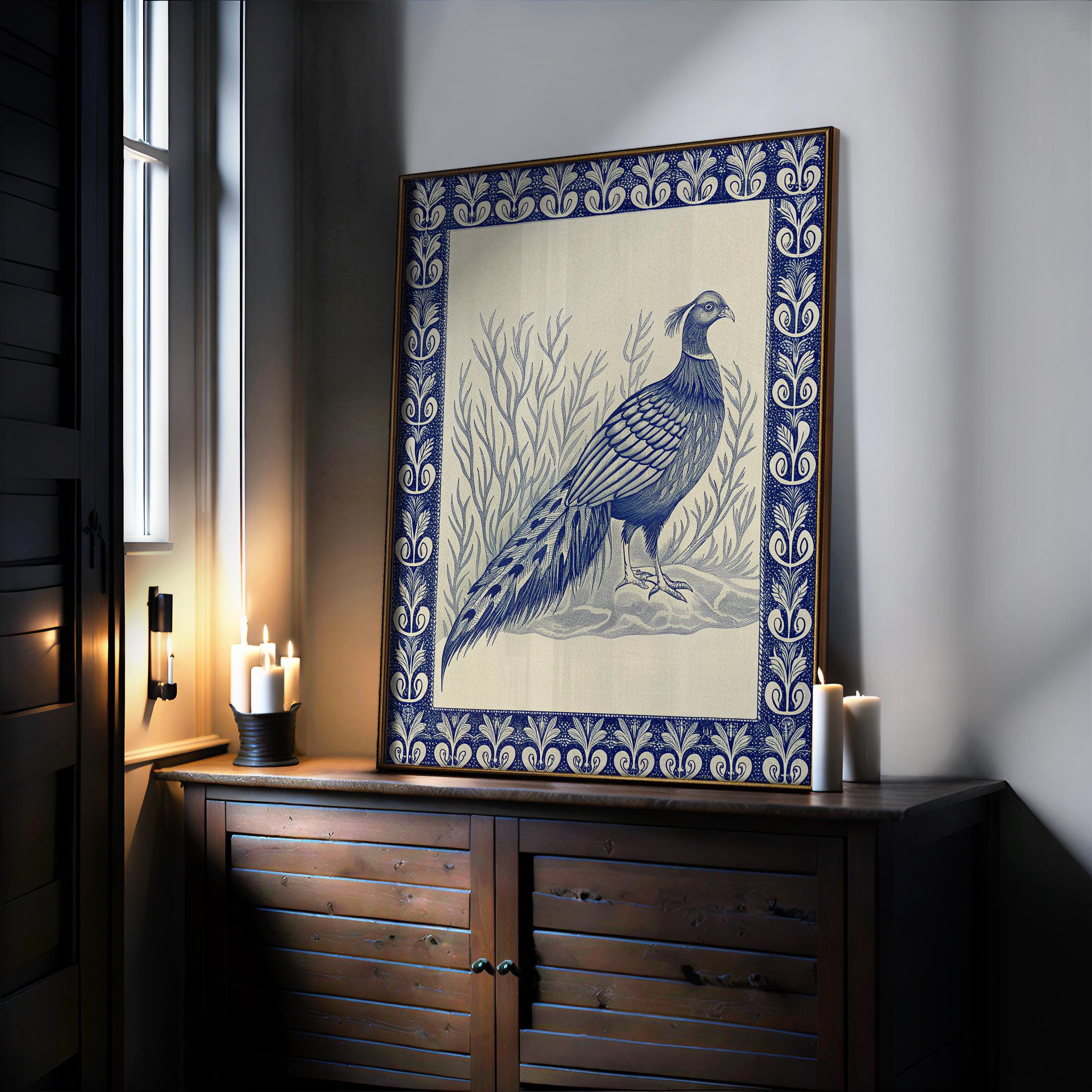A framed indigo pheasant art print with an ornate border sits on a wooden cabinet by lit candles in a softly lit room—Vintage Pheasant Wall Art from West & Wild Art Archive.