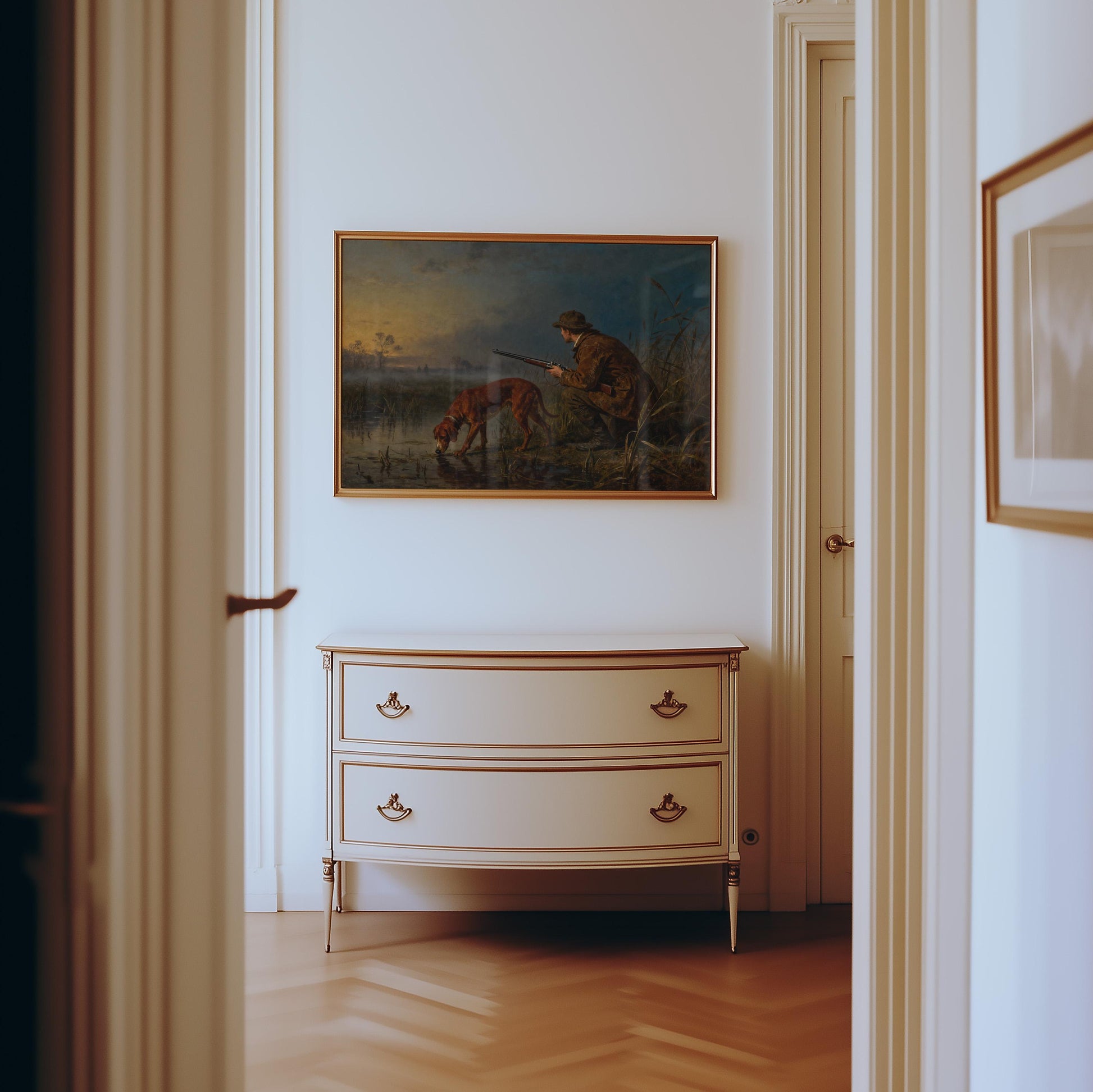 a hallway with a painting of a man and a dog on the wall, a white dresser with two drawers, and a doorway leading to another room.