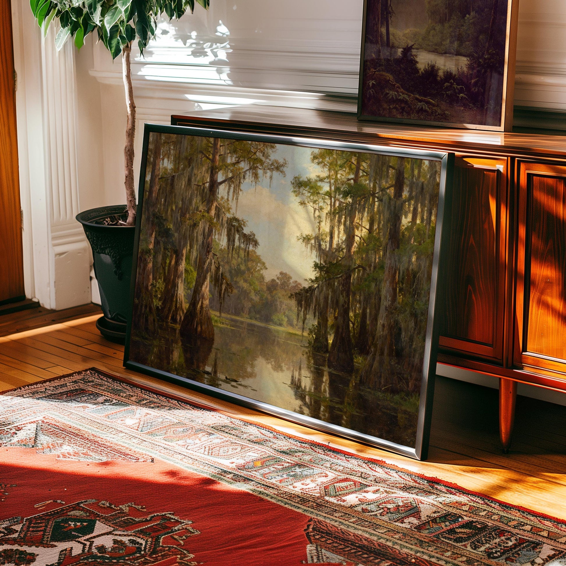 The Vintage Swamp Landscape Print – Cypress Tree Art, a framed nature print from the West & Wild Art Archive, leans against a wooden cabinet on hardwood flooring near a patterned rug and potted plant in a sunlit room.