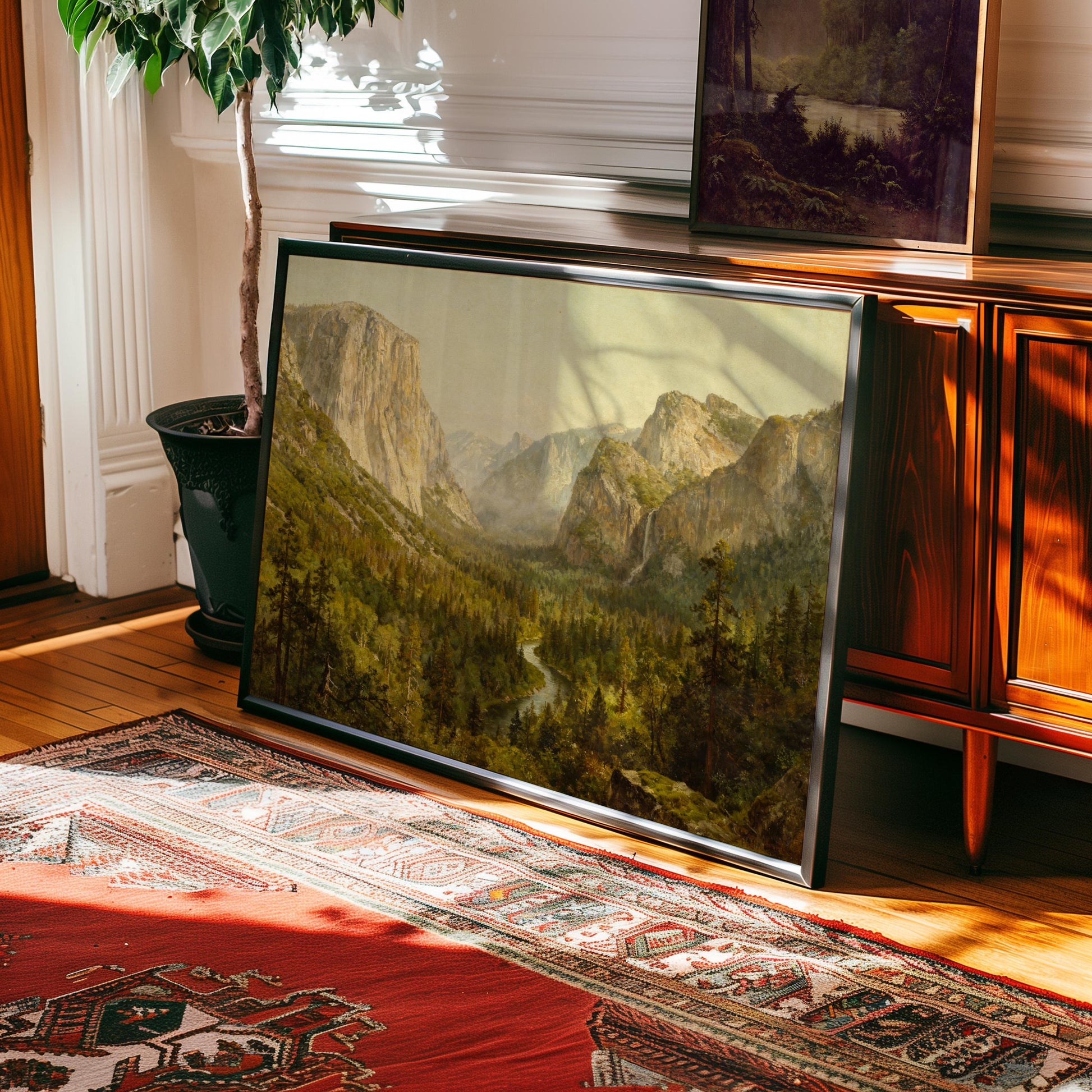 The Yosemite Valley Art Print—Classic American Landscape with River View—is displayed framed against a wooden cabinet near a potted plant; sunlight highlights the Persian-style rug and wooden floor. Part of the West & Wild Art Archive.