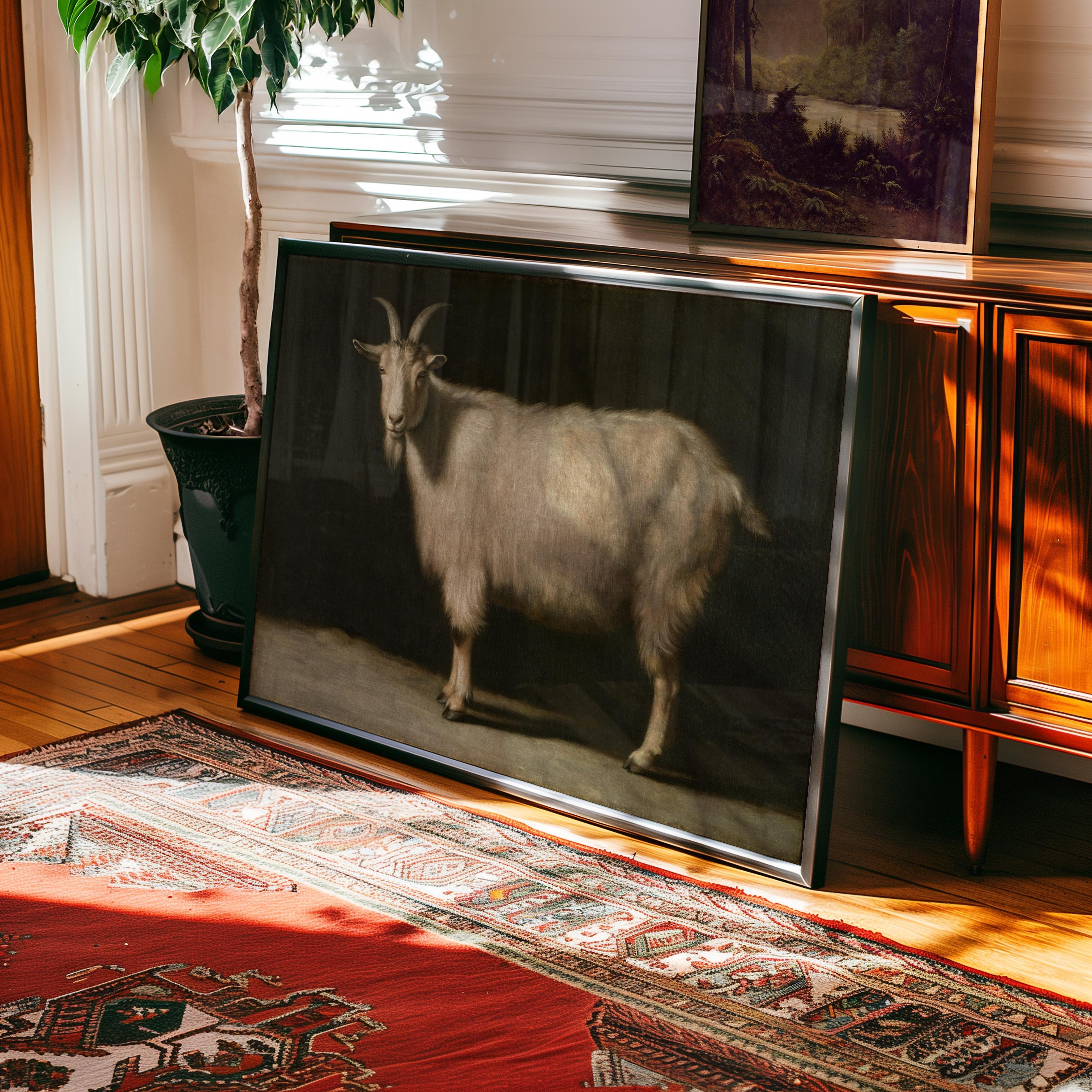 The Goat Portrait Print – Vintage Farm Animal Art | Framed Rustic Farmhouse Decor rests against a wooden sideboard on a sunlit floor, beside a potted plant and rug, with another framed landscape above.
