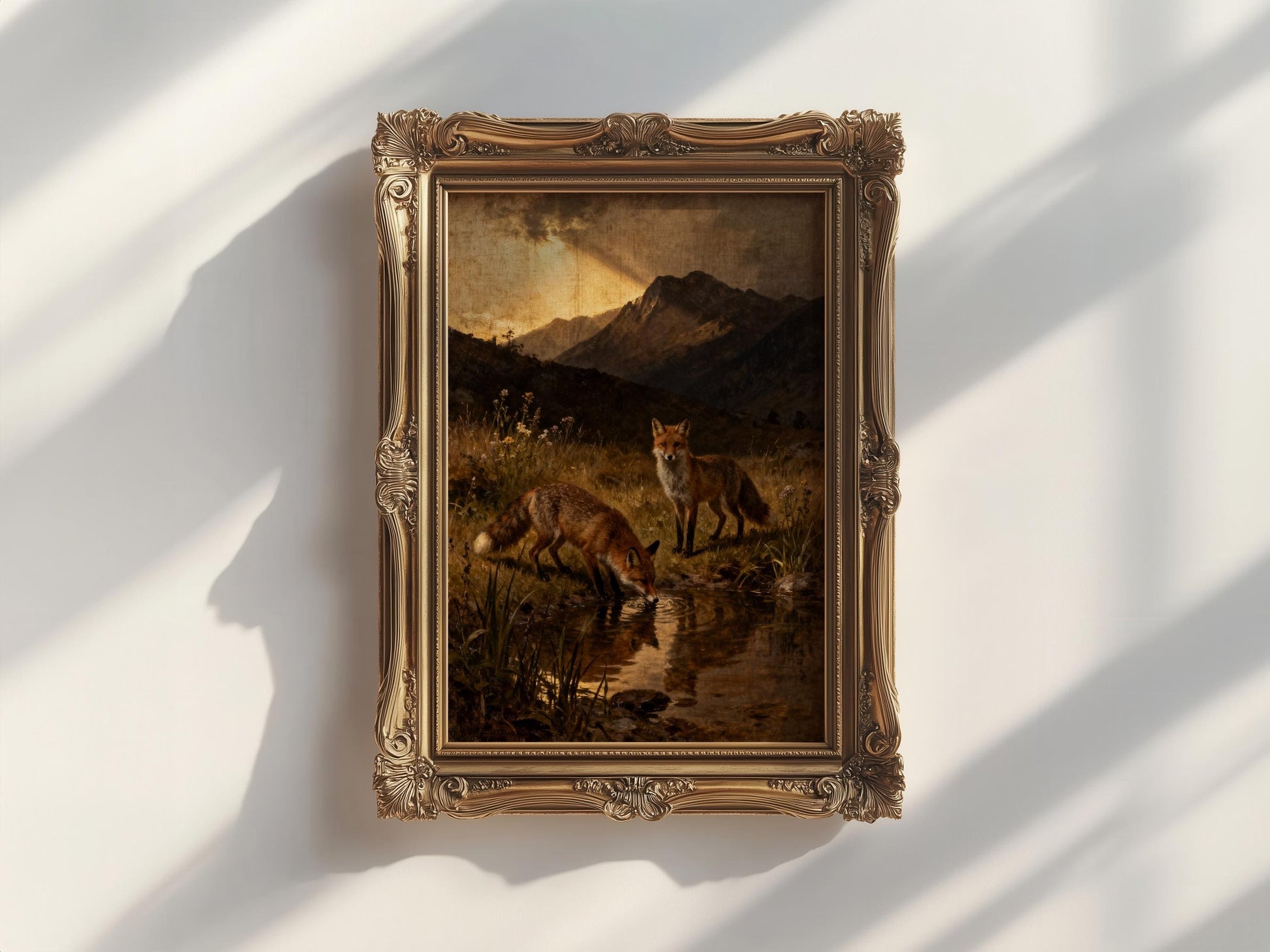 The image is a painting of two foxes in a grassy field, with mountains in the background. The painting is framed in an ornate gold frame and is hung on a white wall.
