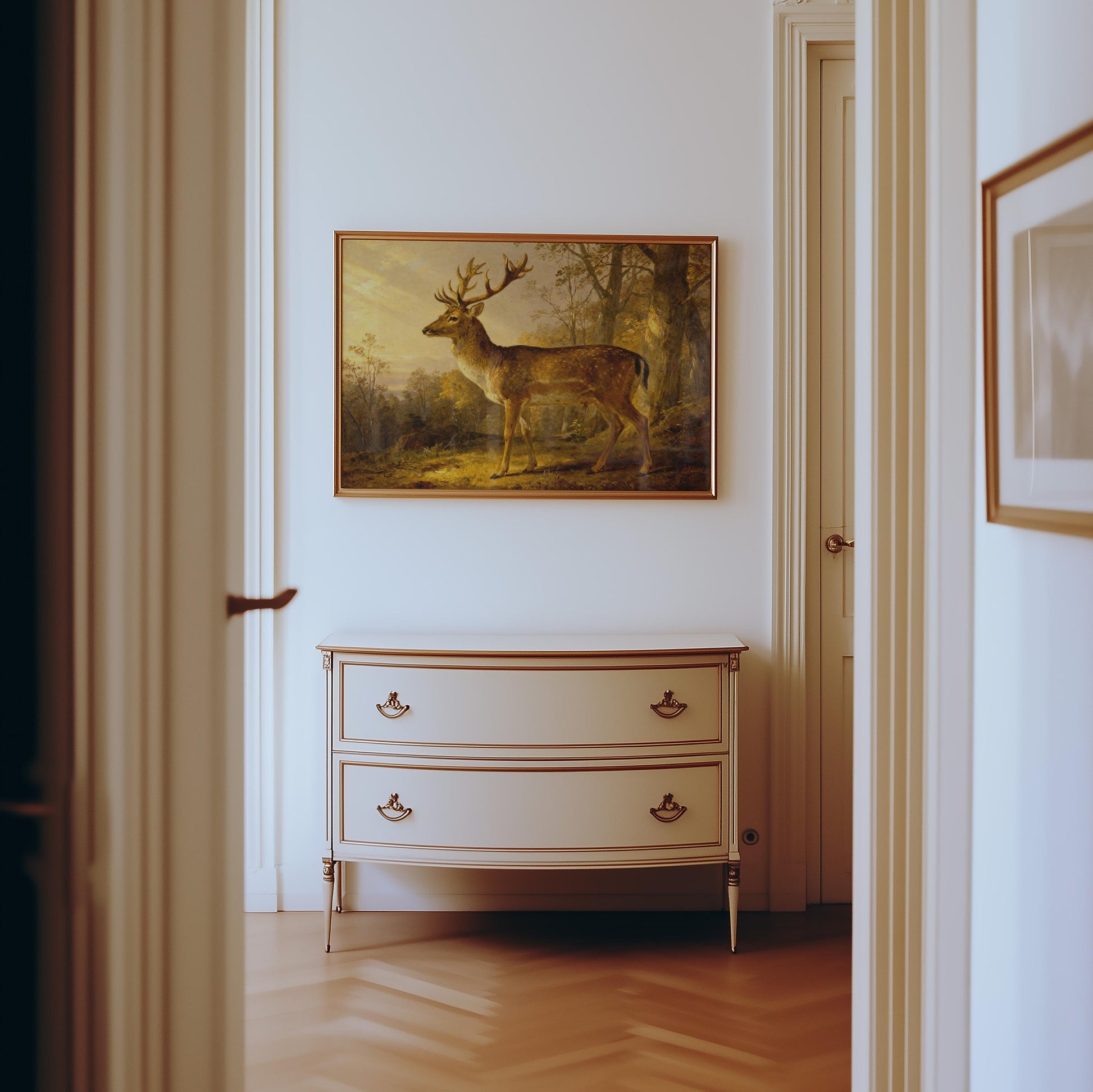 a hallway with a painting of a deer hanging on the wall above a white dresser with two drawers.