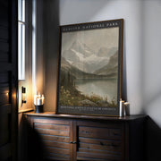 A Glacier National Park Print – Vintage Mountain Landscape Poster with wood or metal frame rests on a sideboard near a window, surrounded by lit candles. The vintage art print shows mountains, a lake, and wildflowers in archival quality.