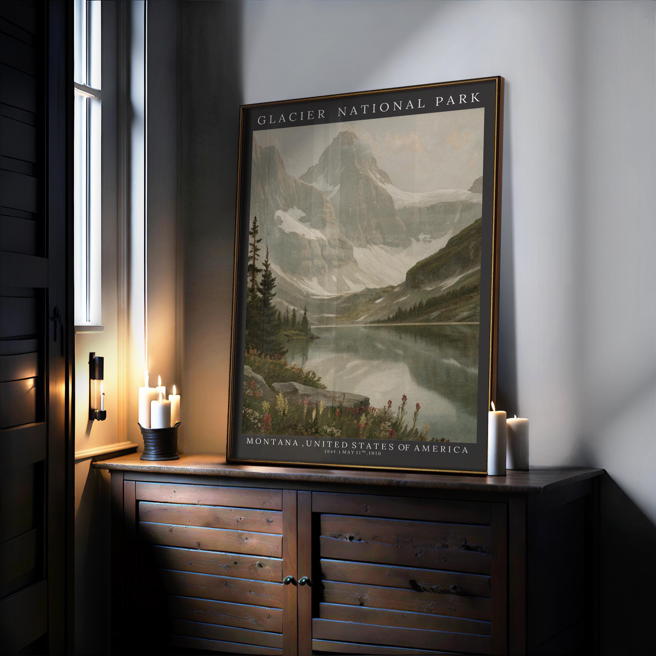 A Glacier National Park Print – Vintage Mountain Lake Scene Framed Wall Decor, featuring mountains, a lake, and pine trees in Montana, USA, is displayed on a wooden cabinet with lit candles and sunlight from a nearby window.