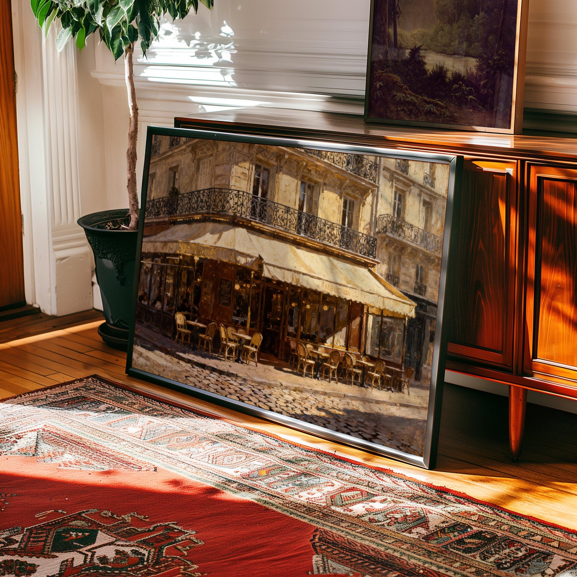 The Vintage Paris Wall Art—Paris Cafe Art Print (framed or unframed)—leans against a wooden cabinet on hardwood floors beside a patterned rug and potted plant, bringing timeless European charm from West & Wild to this sunlit room.