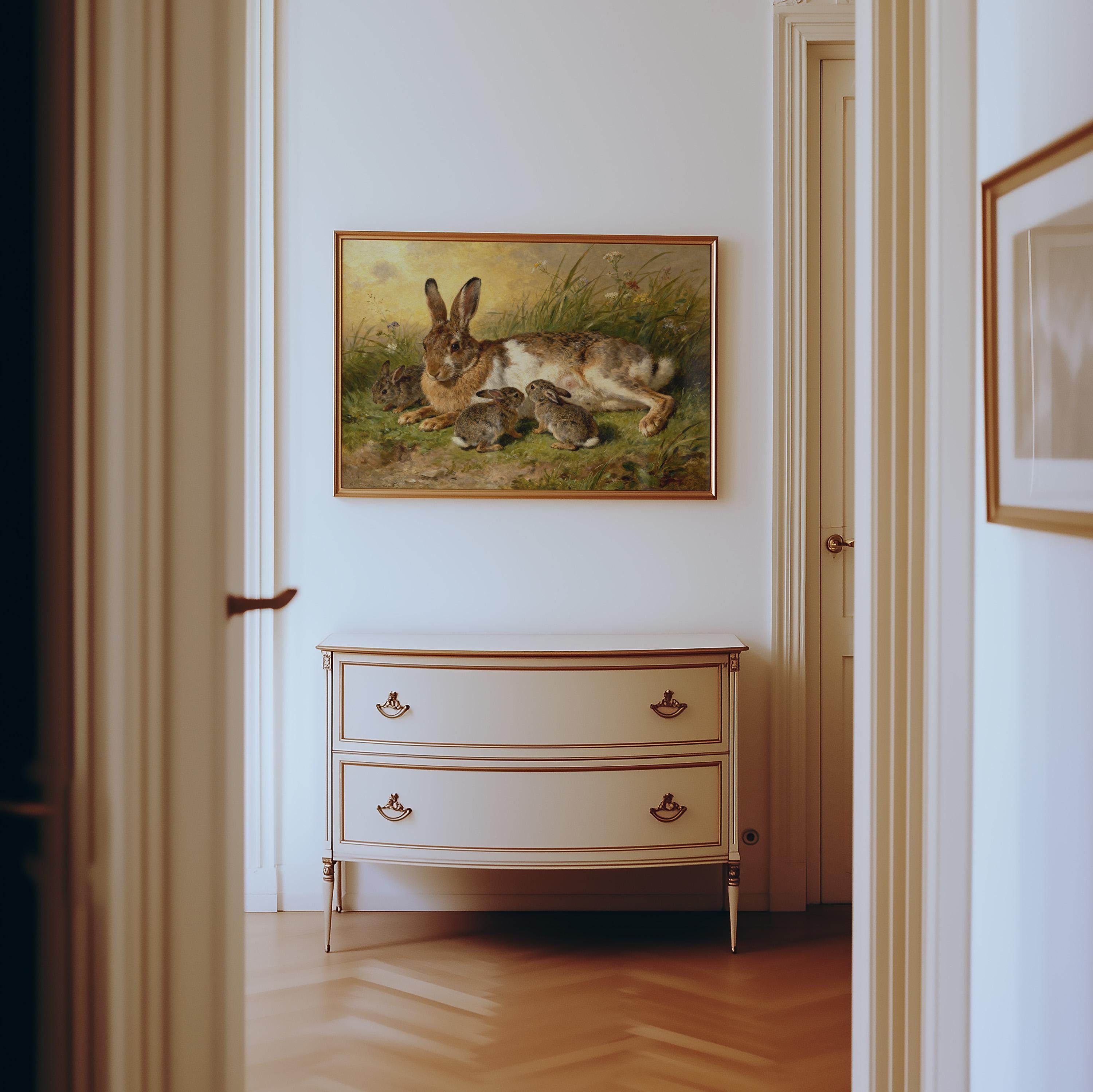 a painting of a rabbit resting in a grassy field, hanging on a white wall above a white dresser with two drawers.