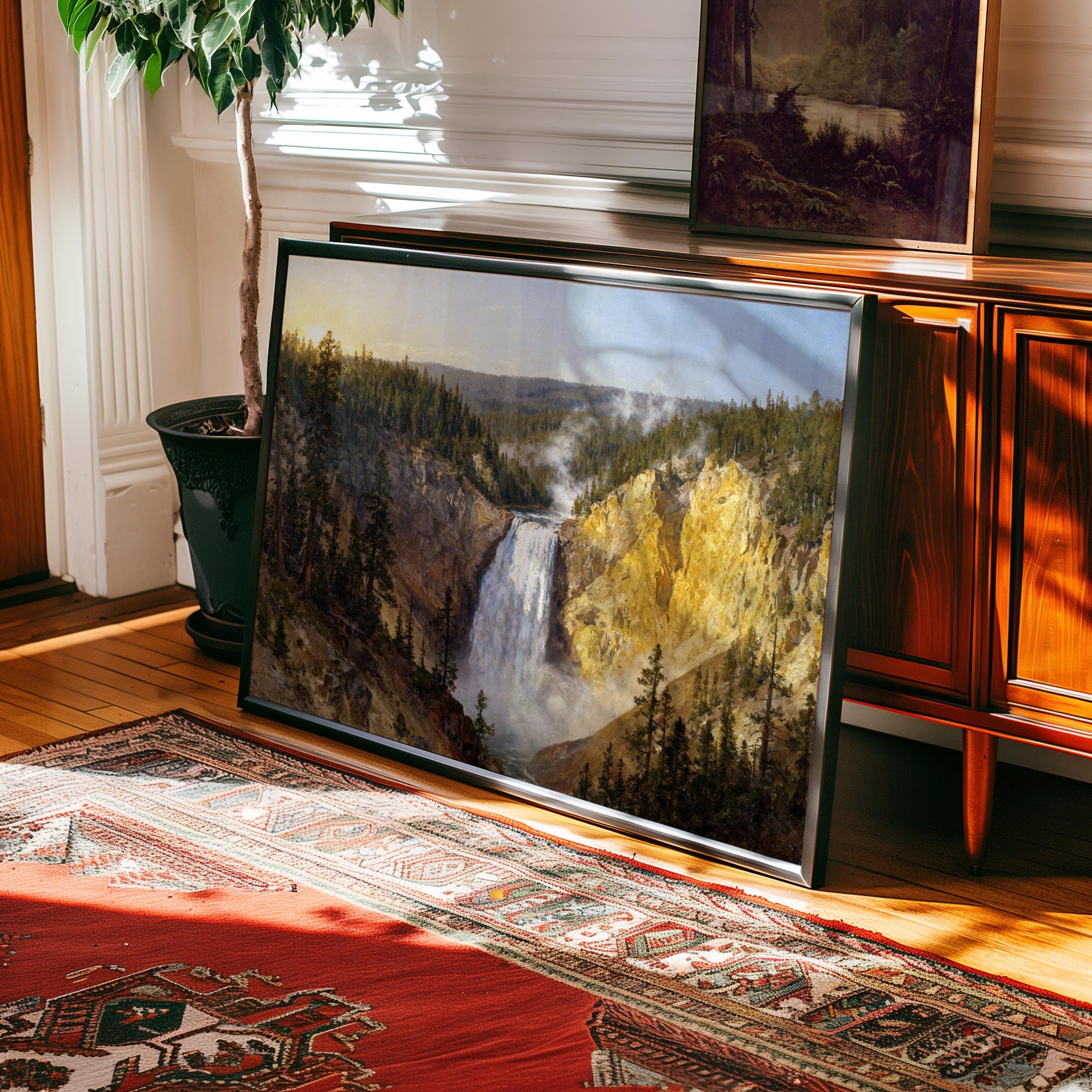 a large framed painting of a waterfall, placed on a rug in a room with a wooden cabinet and a potted plant.