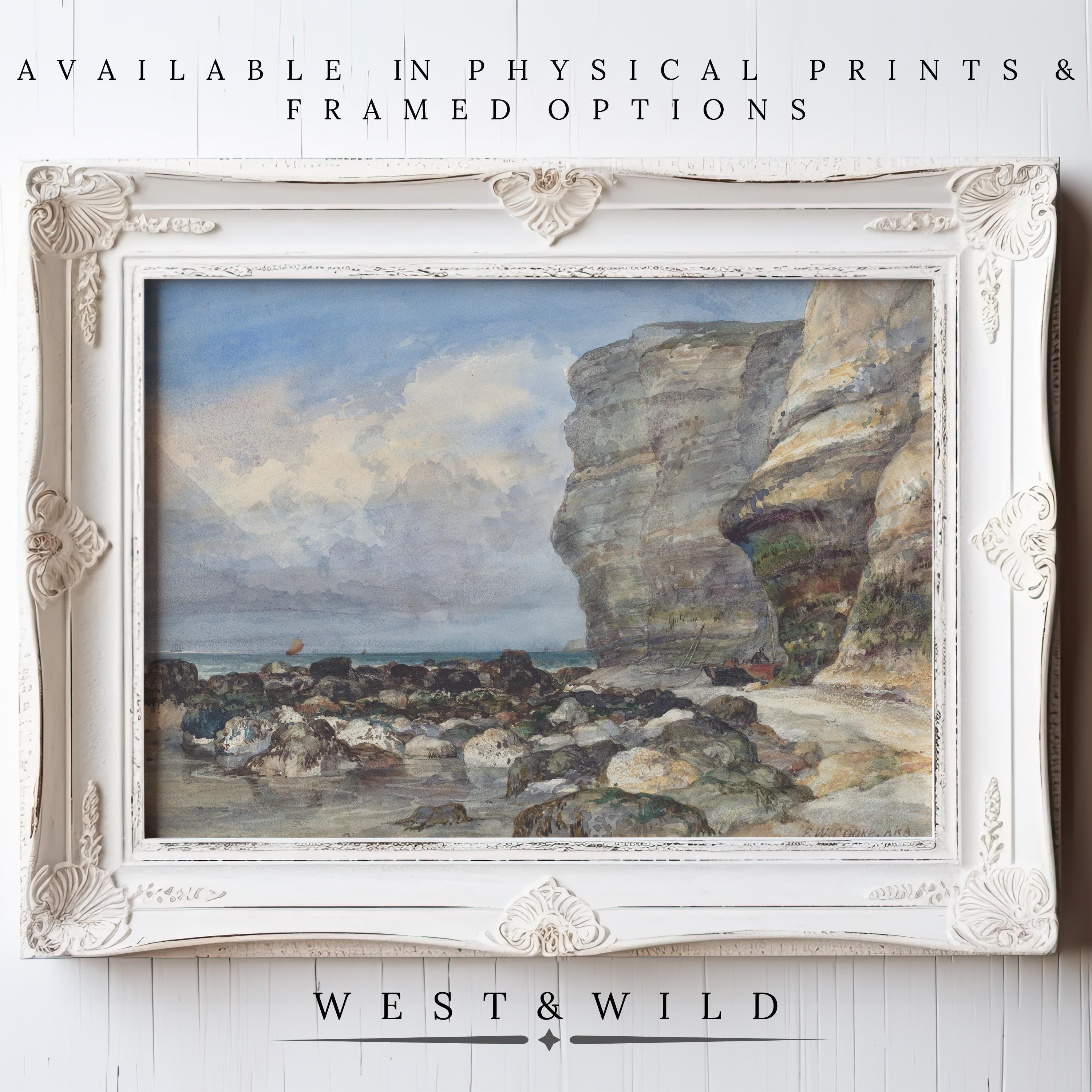 A framed "Coastal Landscape Wall Art - Vintage Beach Painting" featuring a rocky seaside cliff with waves and cloudy sky, displayed on a white wall. Available as vintage art prints & framed art from West & Wild Art Archive.