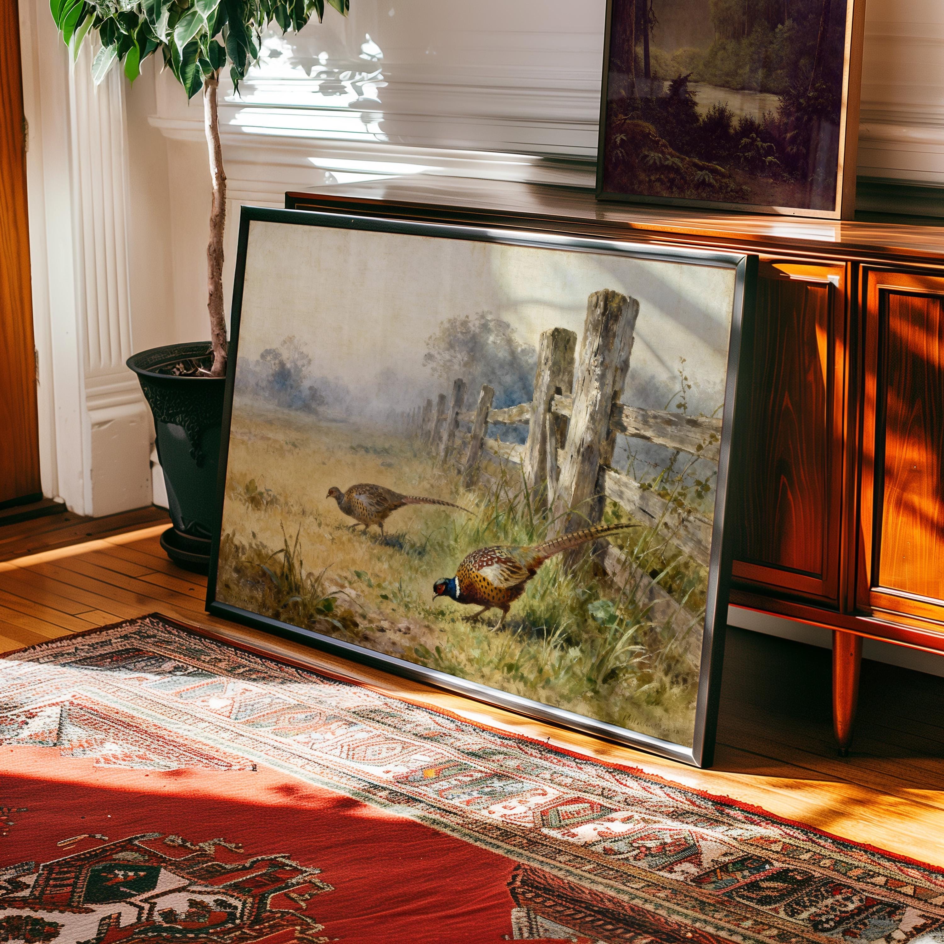 a large painting of two pheasants in a grassy field, with a wooden fence and a tree in the background. The painting is framed and displayed on a wooden cabinet or shelf.