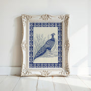 A framed Vintage Pheasant Wall Art print from West & Wild features indigo bird artwork with an ornate white frame, leaning against a white wall on a light wood floor.