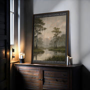 A framed Everglades National Park Art – Framed Wall Art sits on a wooden sideboard by the window, lit by warm candlelight, showcasing vintage nature art of a misty cypress swamp and distant sun.