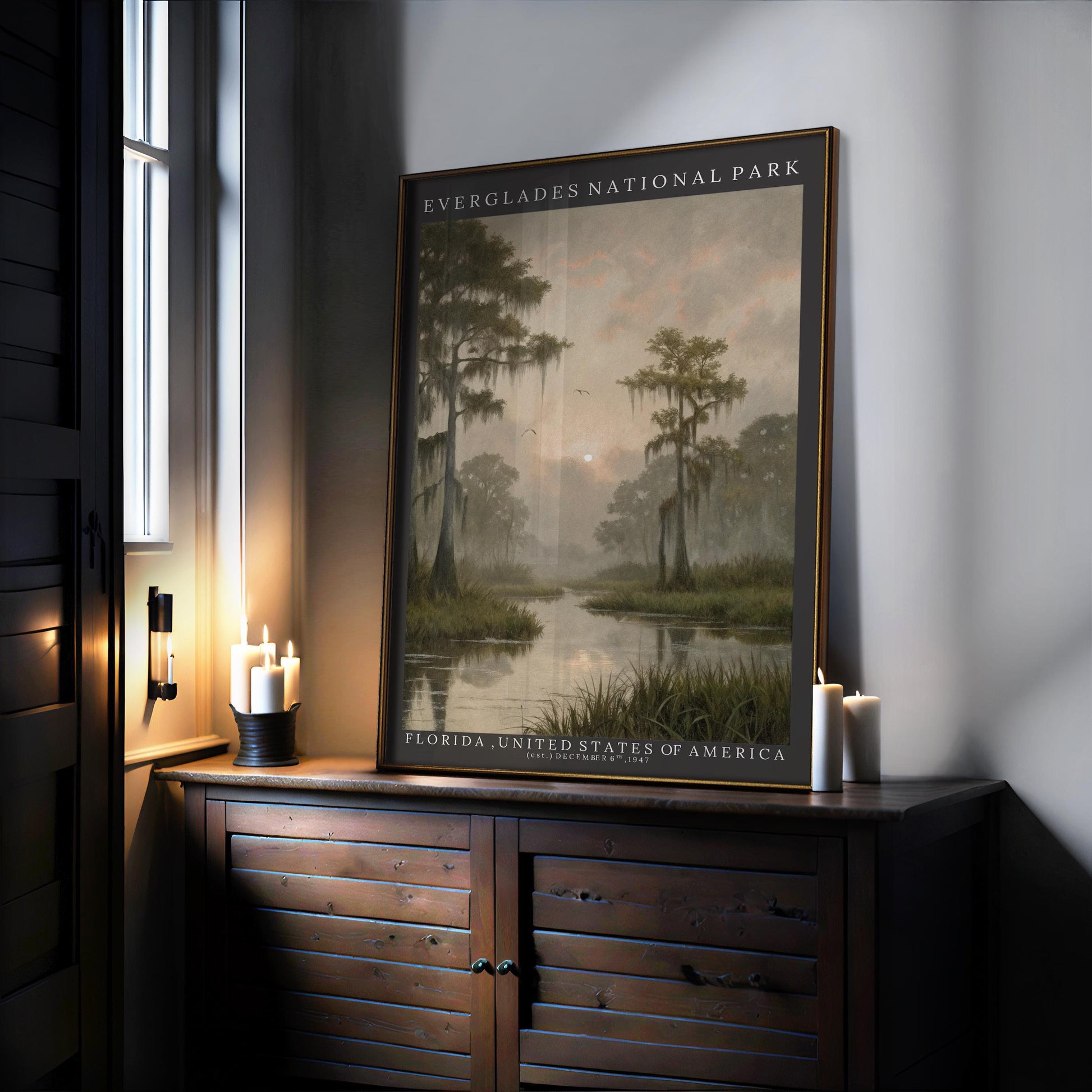 A framed Everglades National Park Art – Framed Wall Art sits on a wooden sideboard by the window, lit by warm candlelight, showcasing vintage nature art of a misty cypress swamp and distant sun.
