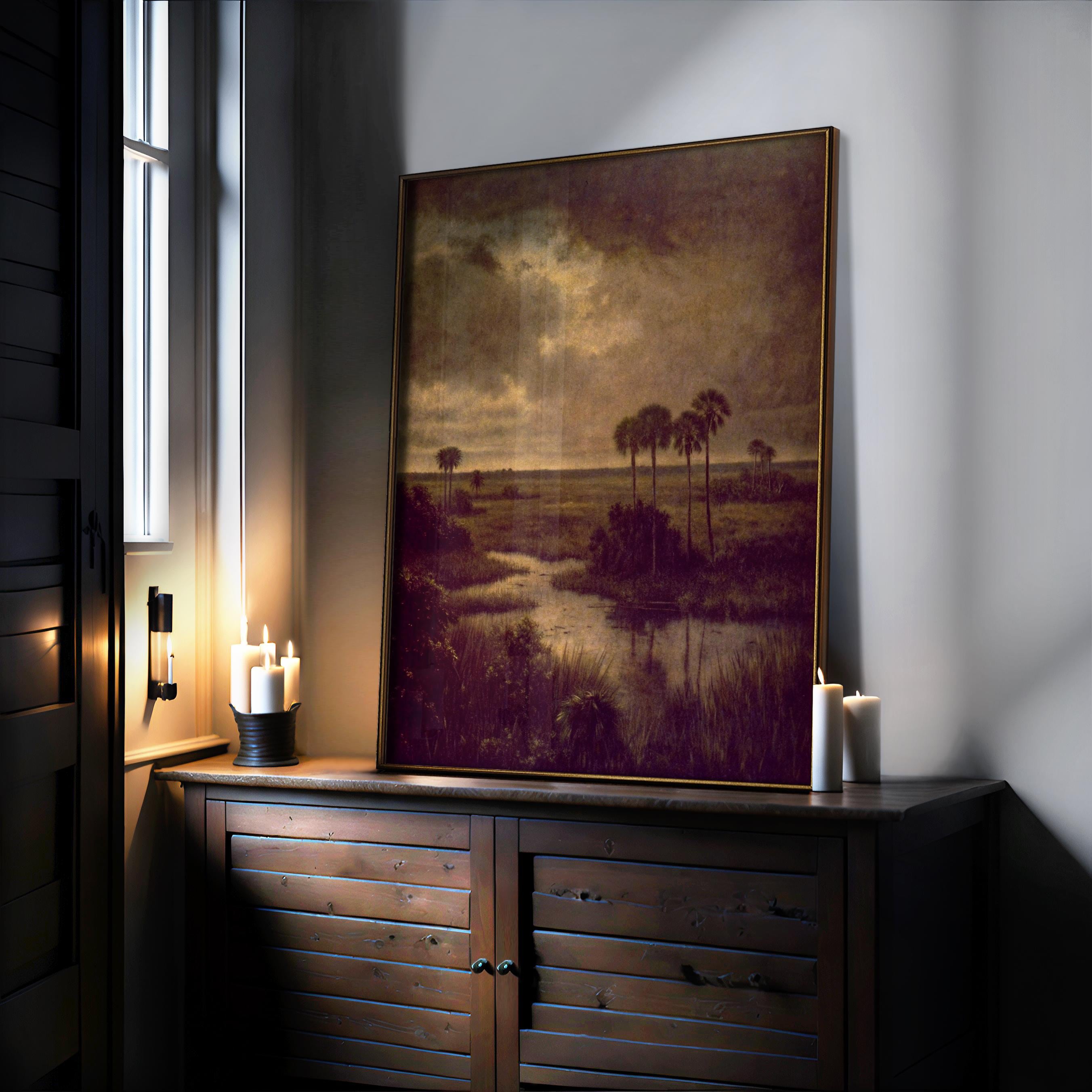 A framed Florida Landscape Print – Tropical Sunset Art With Palm Tree Wall Decor sits on a wooden sideboard surrounded by glowing candles, featuring a moody sky, water, and palm trees that evoke a warm, cozy atmosphere.