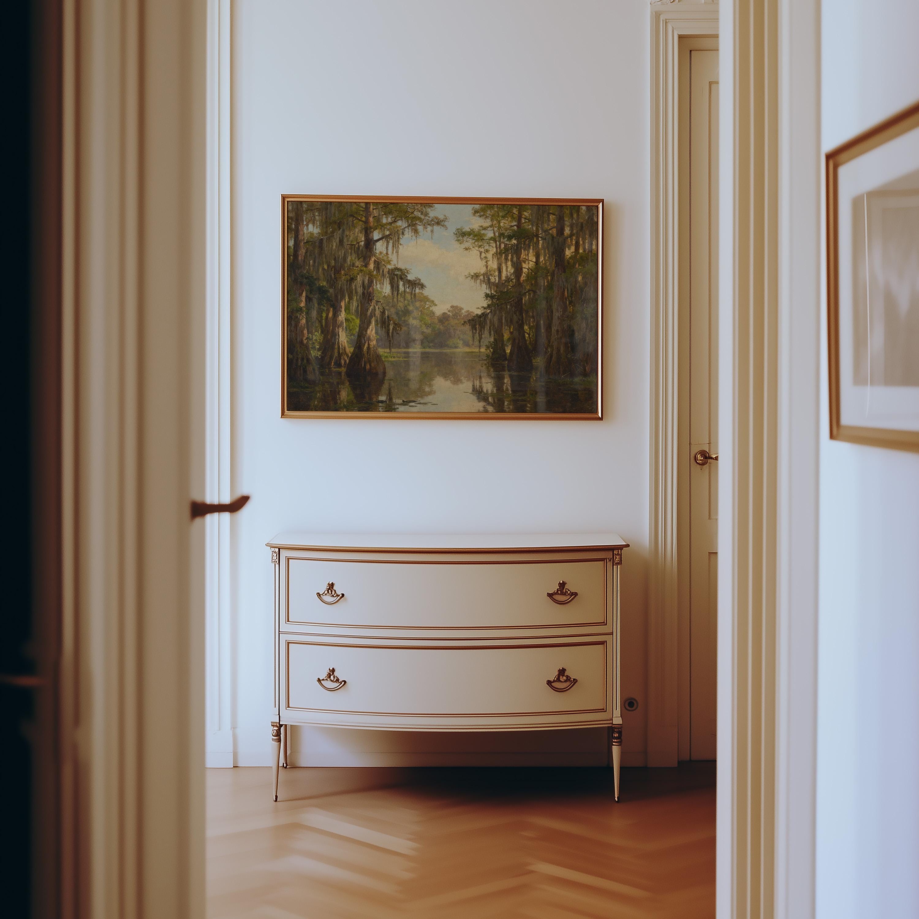 A classic wooden dresser with gold handles stands against a white wall beneath a Vintage Swamp Landscape Print – Cypress Tree Art, in a bright hallway with light wood flooring and elegant white trim.