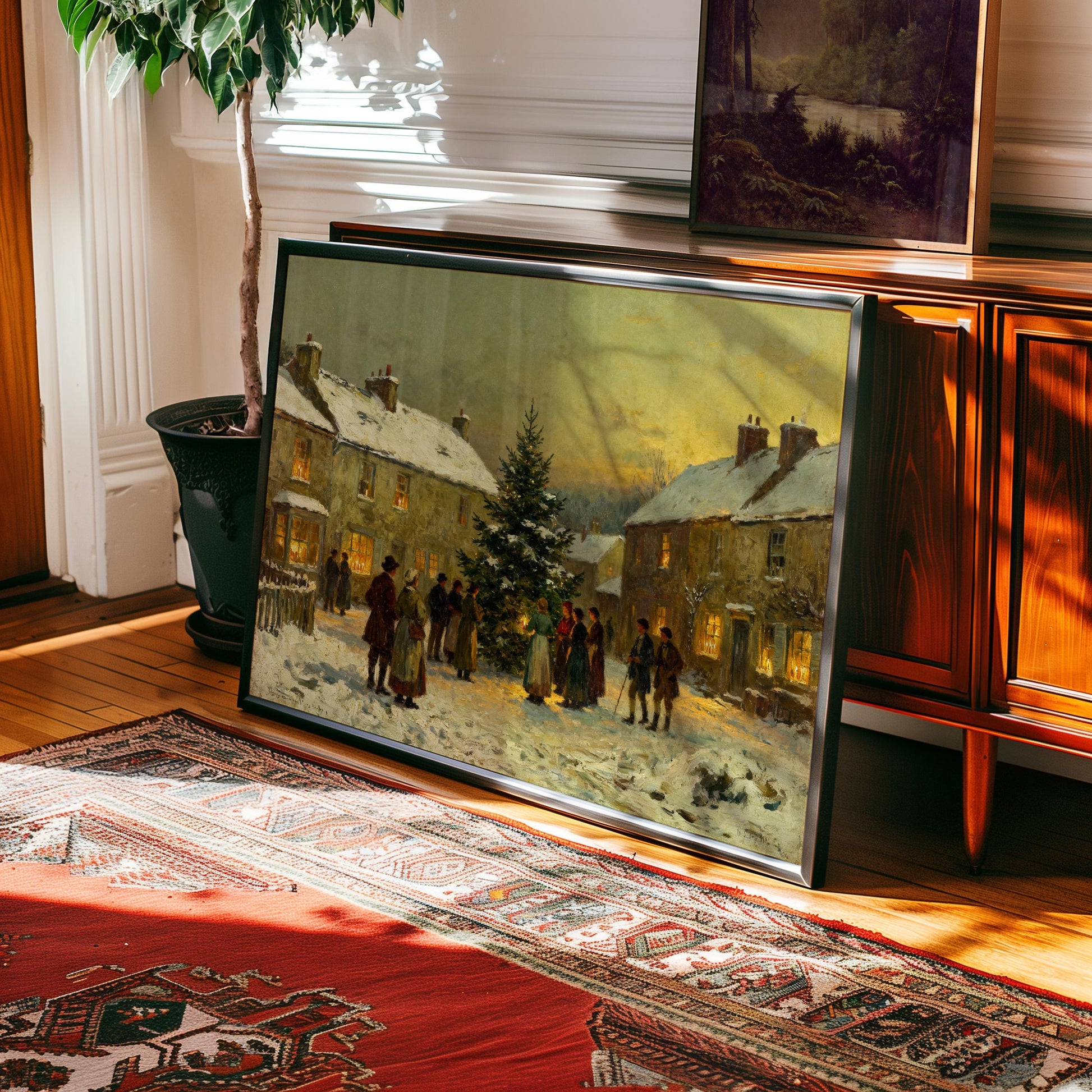 The Village Christmas Tree Art – Classic Holiday Winter Scene Wall Art (framed) is displayed against a wooden cabinet near a potted plant and red rug in a sunlit room, adding vintage charm to your holiday decor.