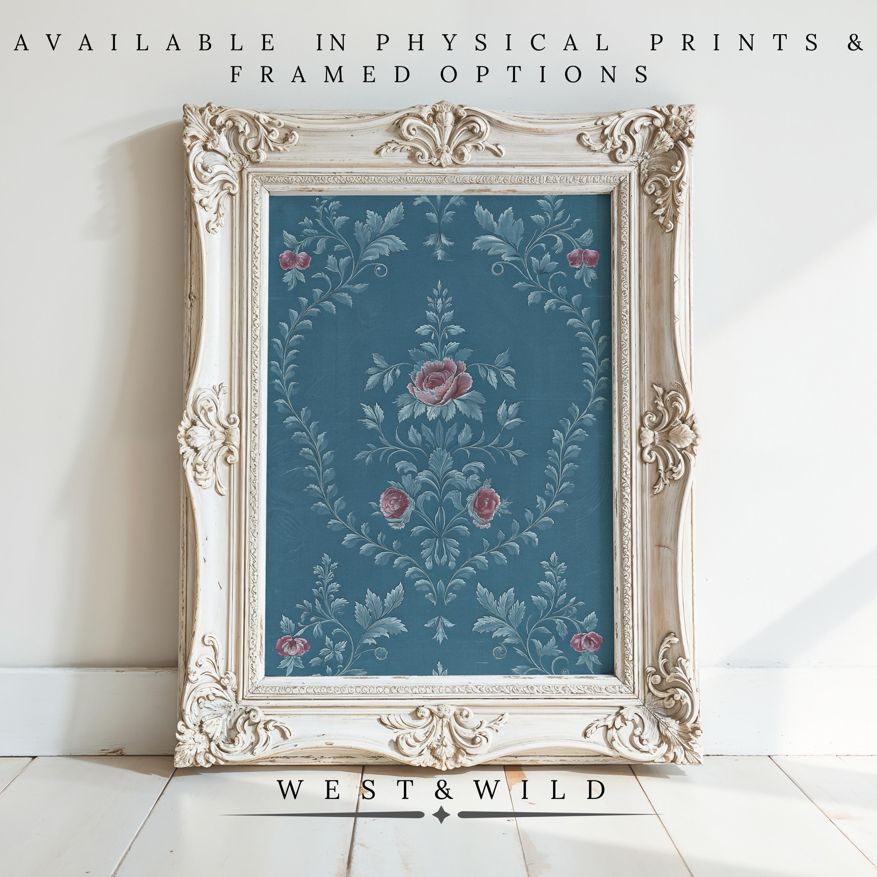 A vintage-style white frame displays the Teal Floral Wallpaper Vintage Wallpaper Print with blue botanicals and pink roses, leaning against a white wall on a wooden floor. Available as physical prints & framed options. West & Wild.