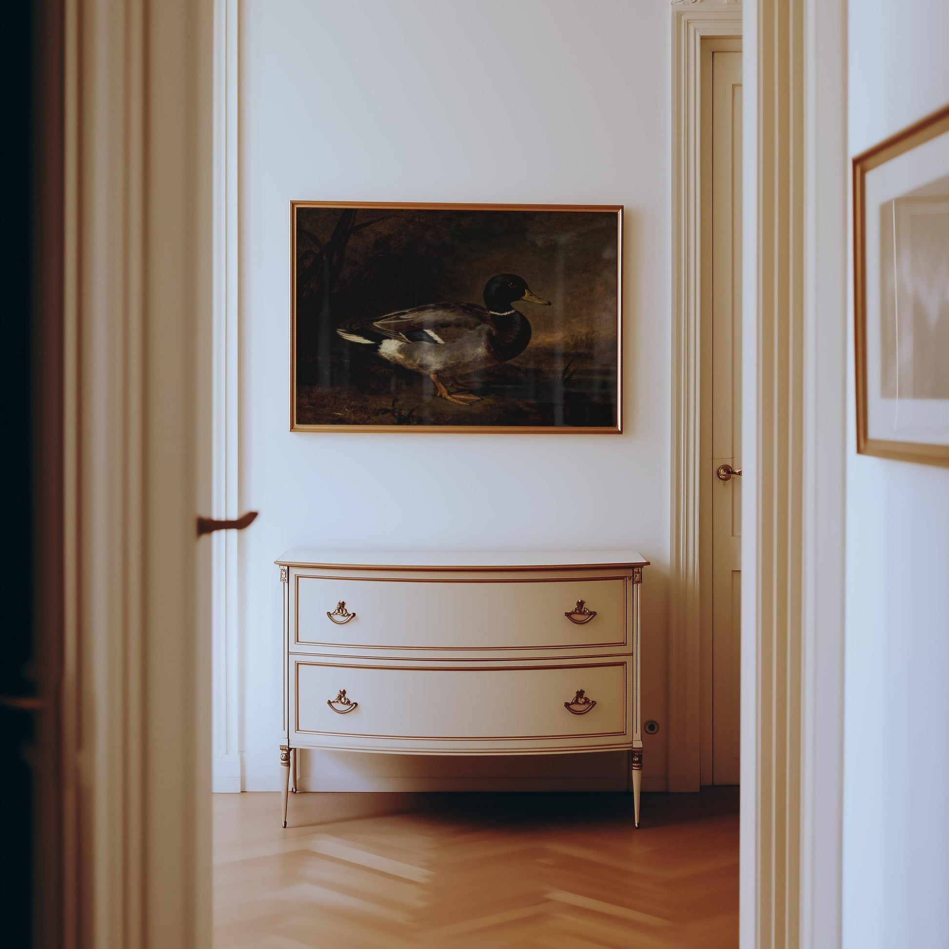a hallway with a white dresser and a framed painting of a duck hanging on the wall above it.