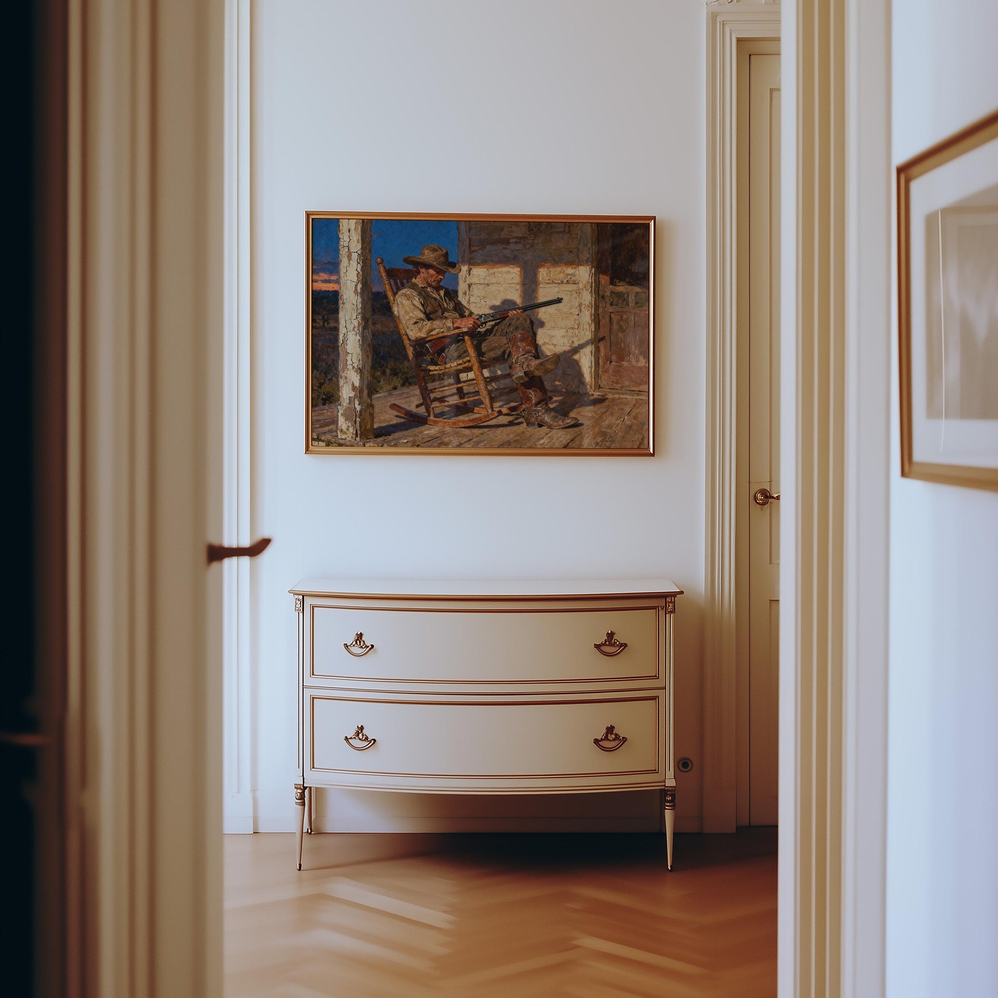 a hallway with a painting of a man sitting in a rocking chair on the wall, and a white dresser with two drawers below it.