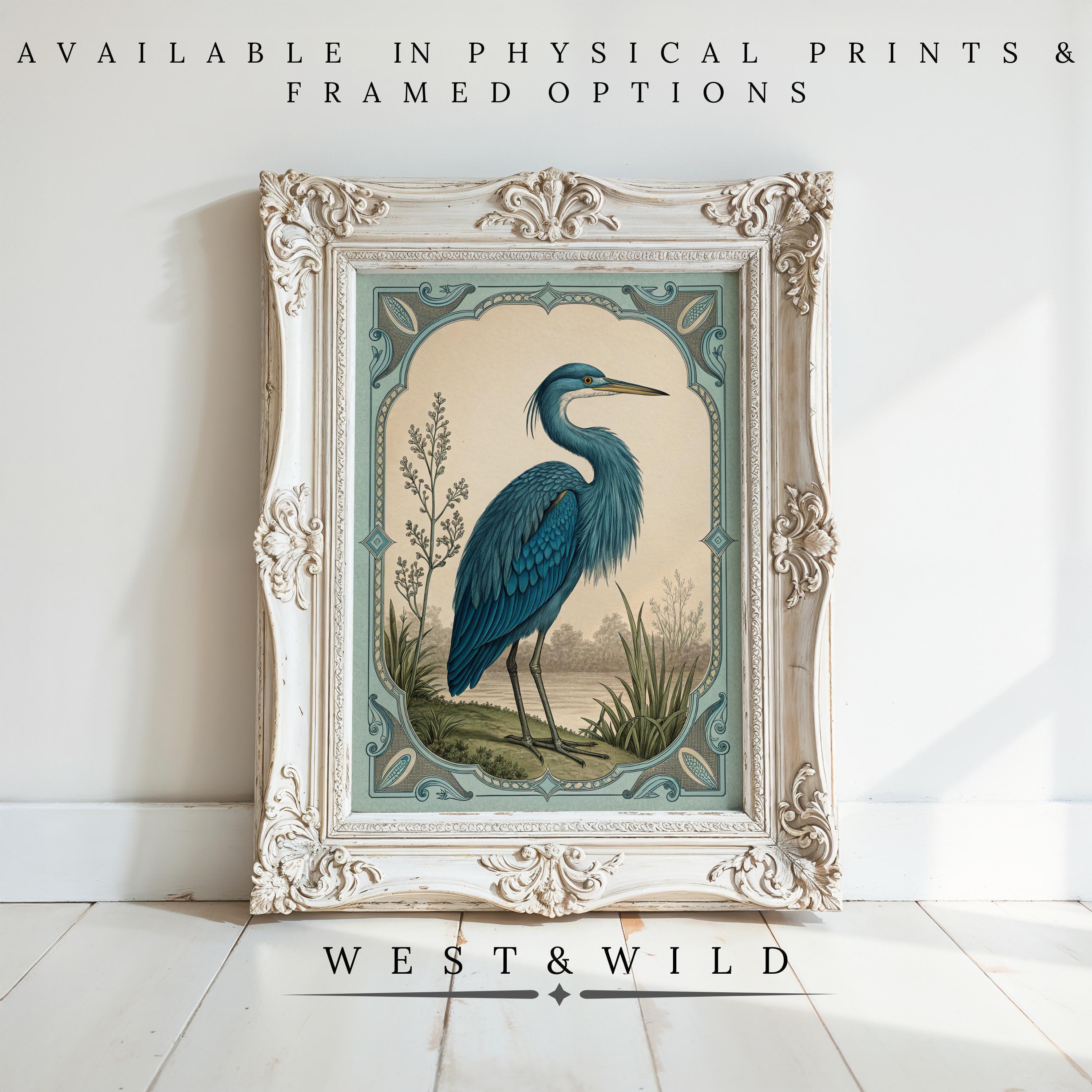 The Blue Heron Painting - Vintage Art Print | Rustic Cabin Decor & Mountain Wall Art is displayed on a light wood floor with greenery. Available as physical prints and framed art from the West & Wild Art Archive.