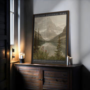 A Glacier National Park Print – Vintage Mountain Valley Scene | Framed Nature Art sits on a dark wooden cabinet near candles and a window, displaying mountains, lake, and trees with “Montana, United States of America” below.