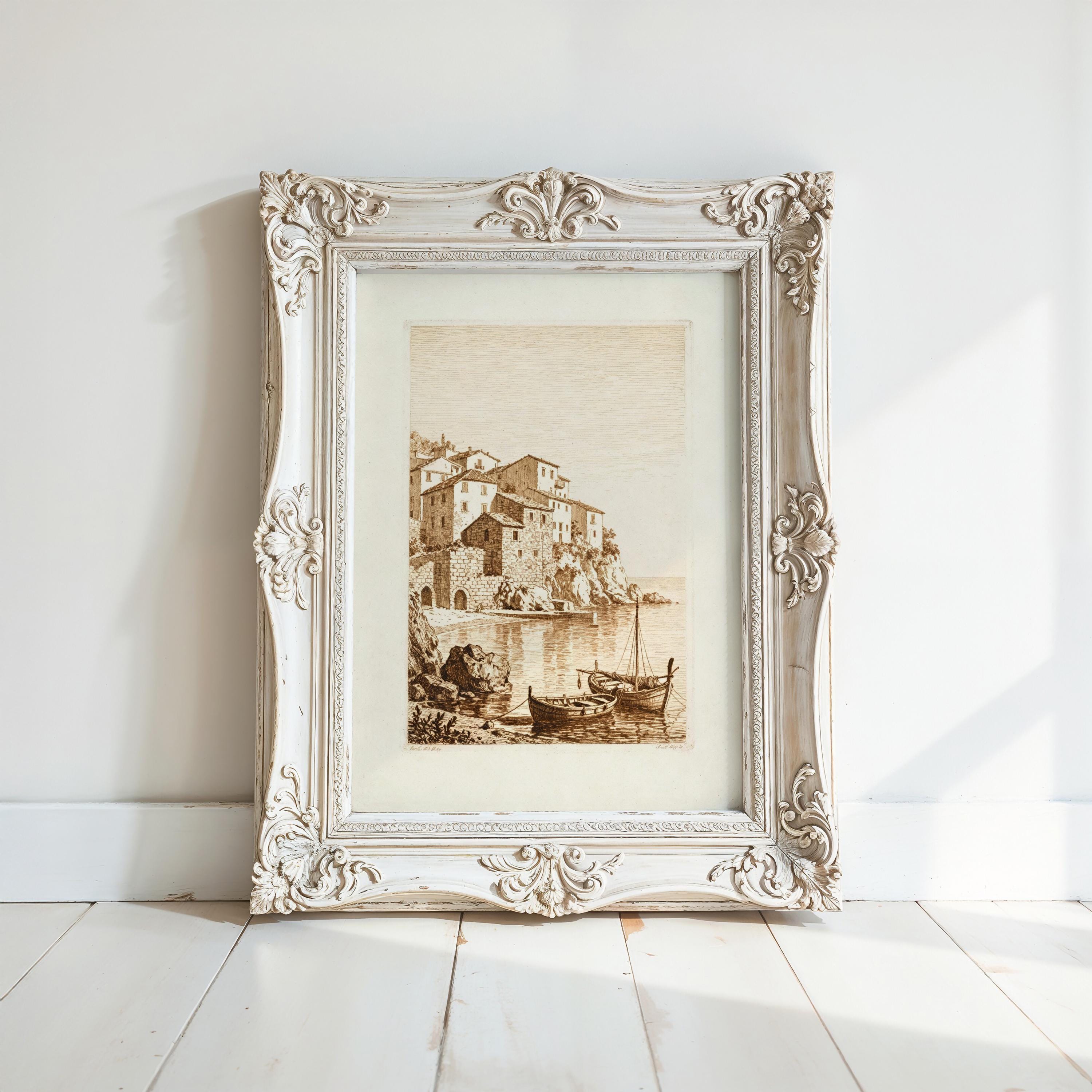 A white ornate picture frame with a painting of a coastal town scene inside it, displayed on a white wall.