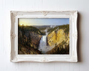 A framed painting depicting a scenic waterfall surrounded by lush green trees and a mountainous landscape.