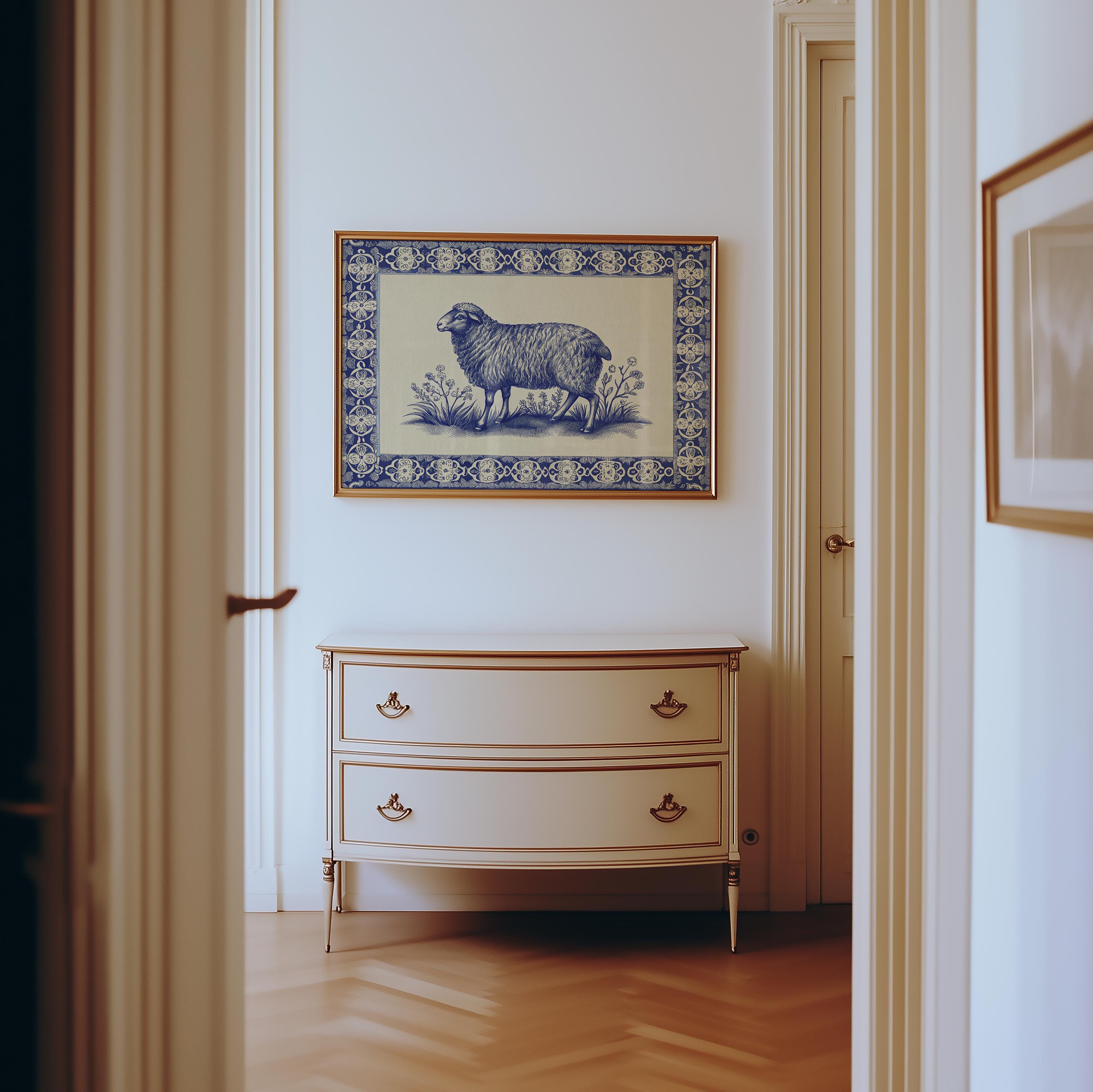 A hallway with light walls features a cream dresser with gold handles. Above it hangs the Framed Sheep Print – Blue China Pattern Rustic Wall Art, ornately framed. The floor is light wood in a herringbone pattern.