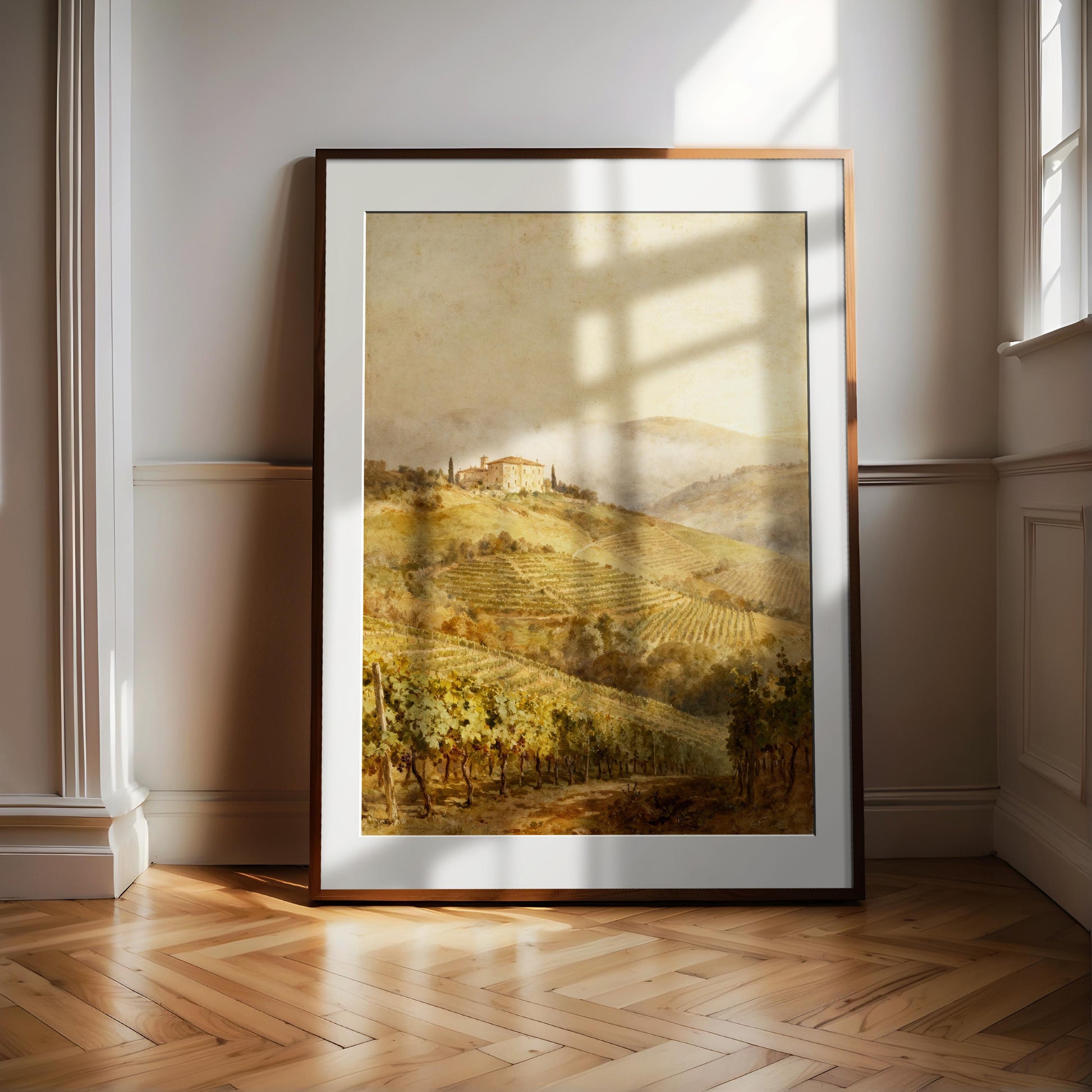 a large framed painting of a countryside landscape, with rolling hills, vineyards, and a small building in the distance. The painting is displayed on a wooden floor, with sunlight streaming in from a window in the background, creating a warm and inviting atmosphere.