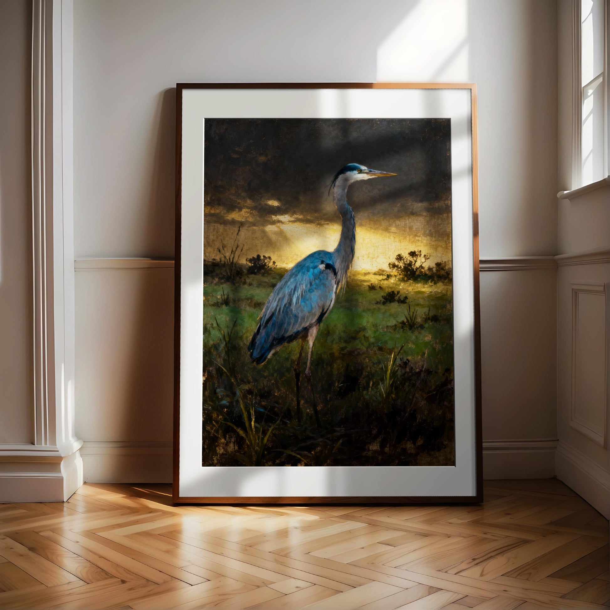 A framed painting of a blue heron standing in a grassy field with a sunset in the background.