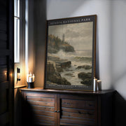 A framed Acadia National Park Poster—Vintage Otter Cliffs Illustration with coastal pines—rests on a wooden cabinet by lit candles and a sunlit window.