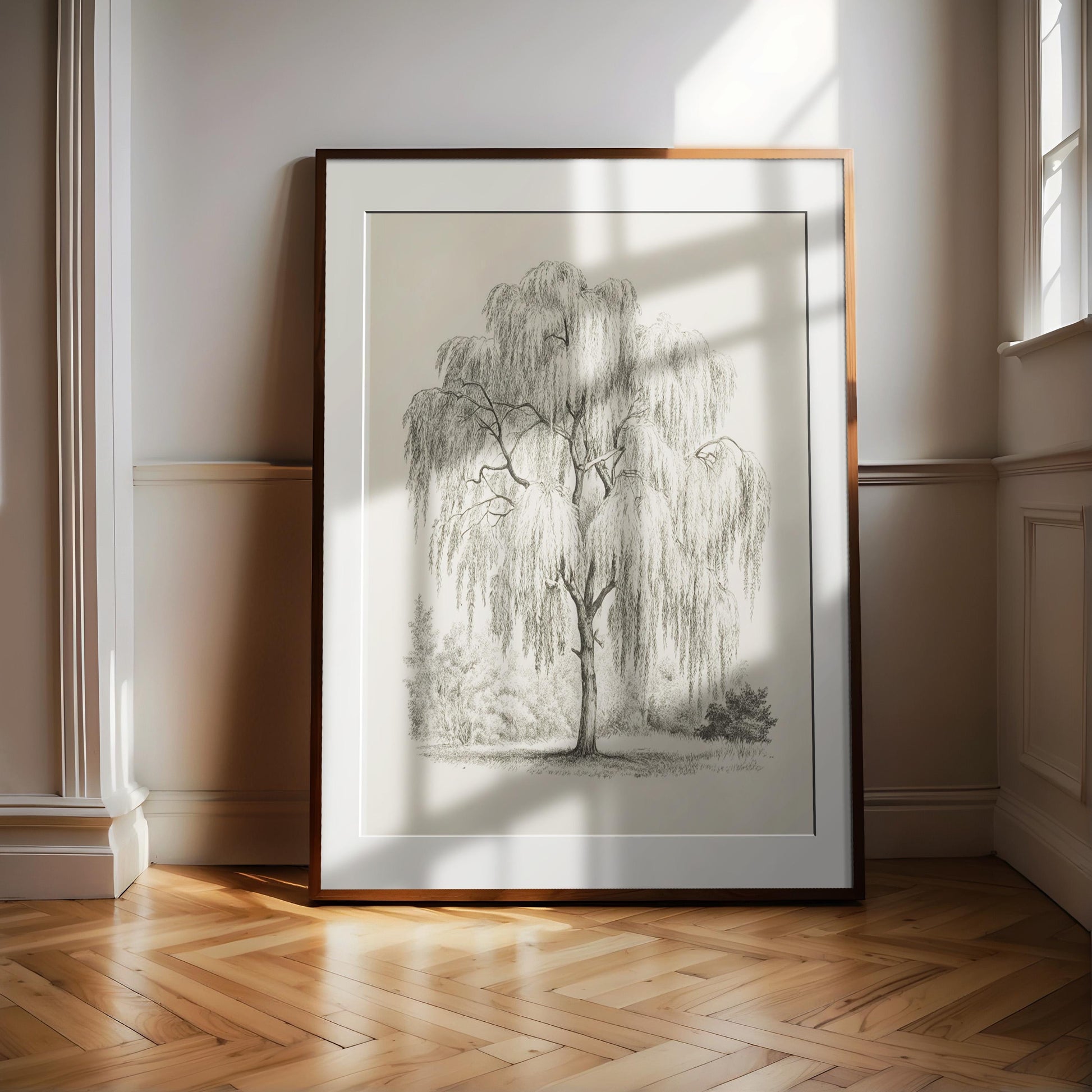 A large framed drawing of a willow tree with long, drooping branches is displayed on a wooden floor in a room with white walls.
